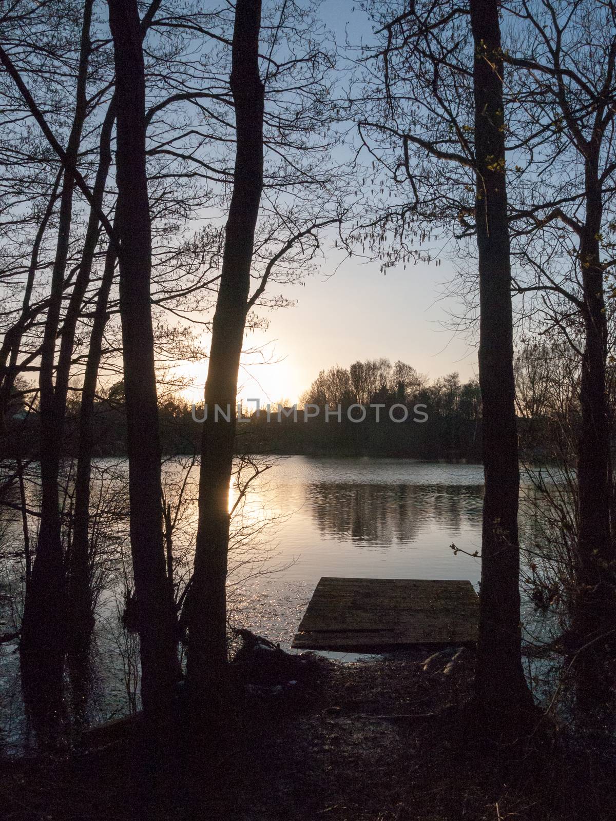 small pontoon of lake water surface with trees and sunset by callumrc