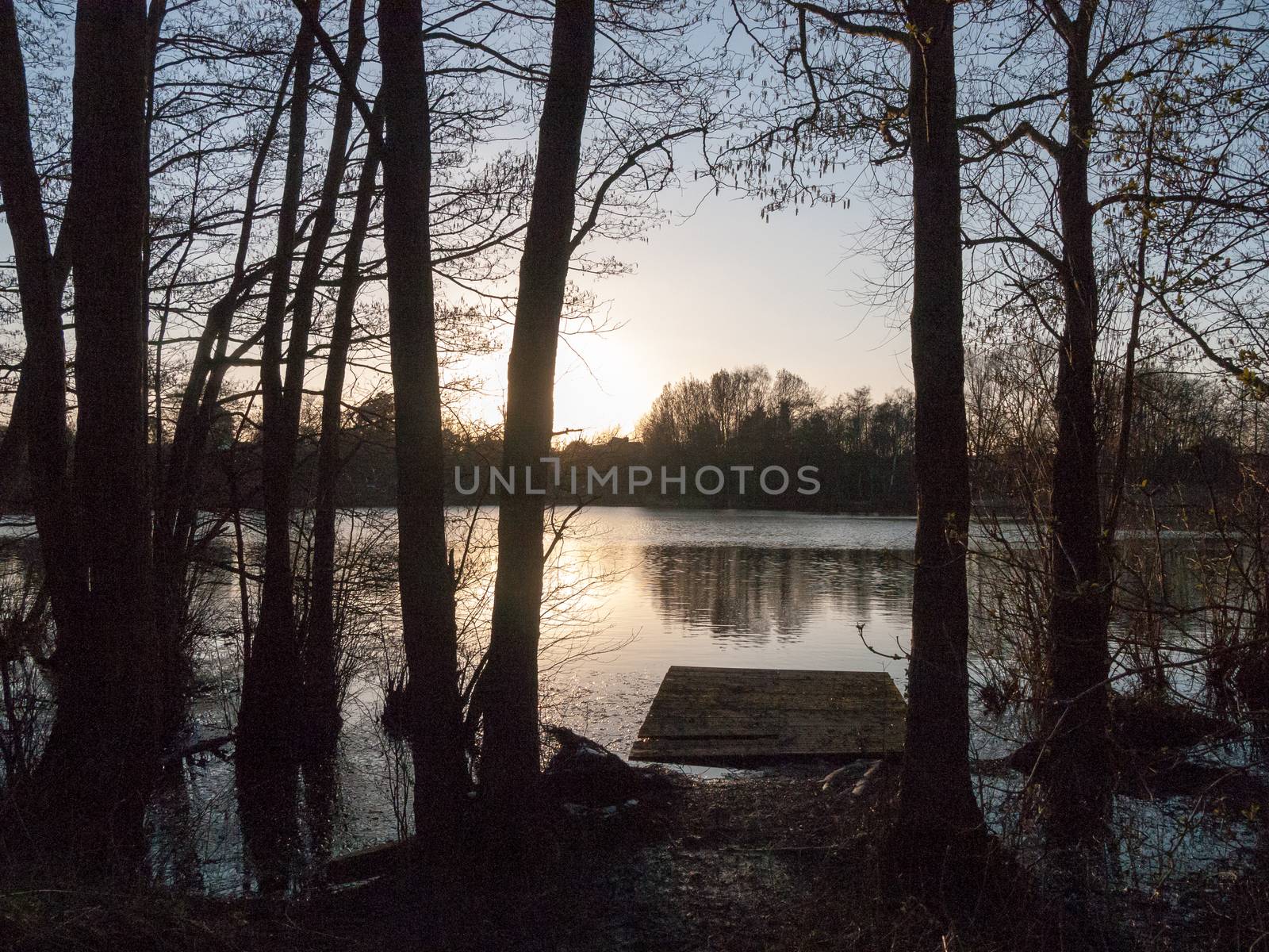 small pontoon of lake water surface with trees and sunset by callumrc