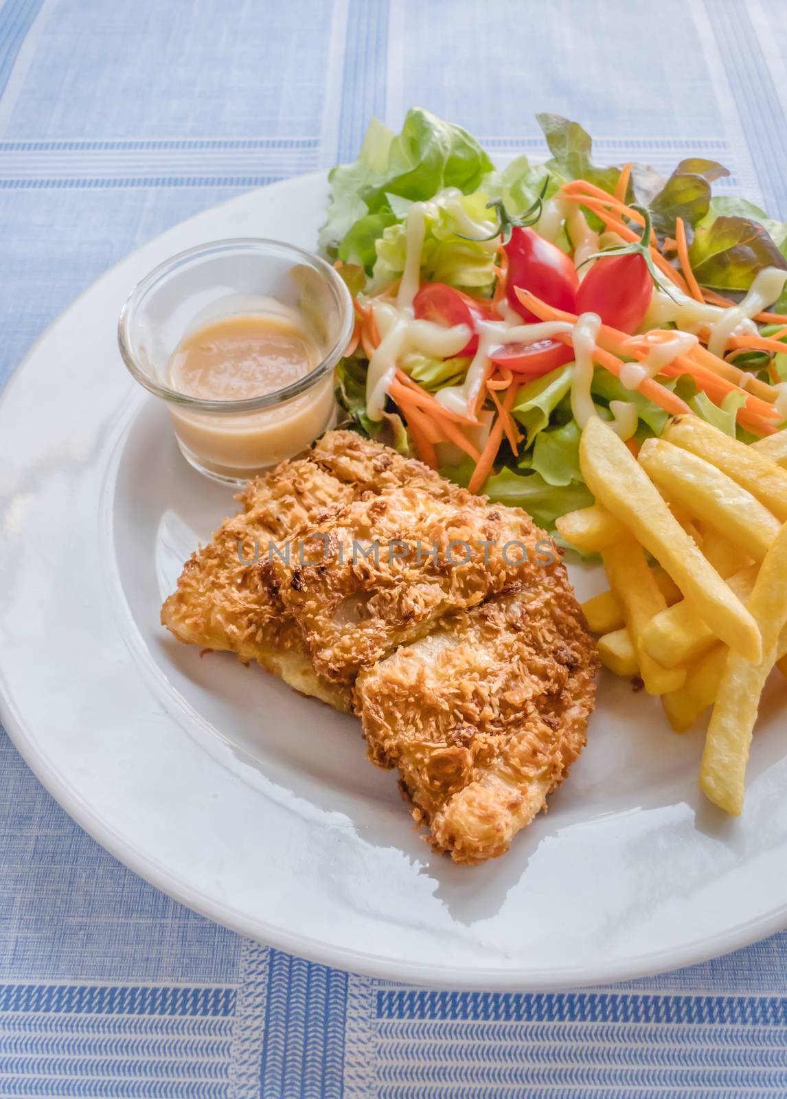 Deep fried fish steak served with french fries and fresh vegetables on white plate