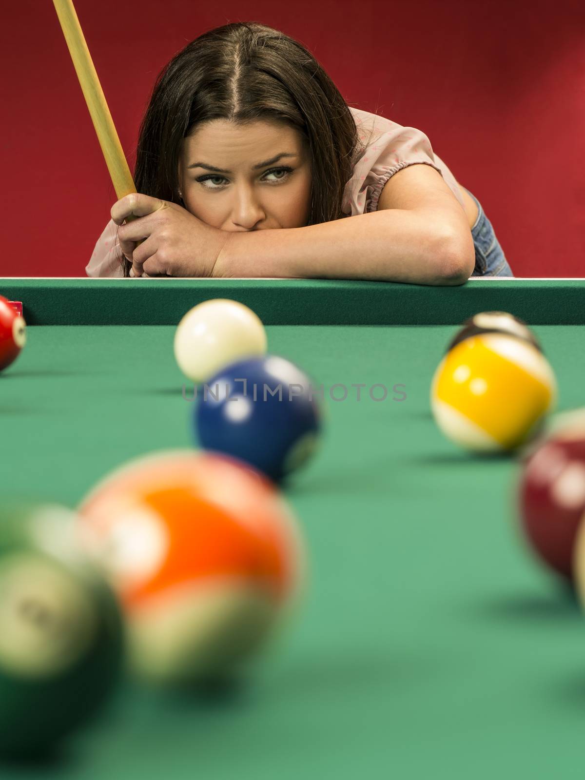 Photo of a beautiful brunette at the edge of a billiards table holding a pool cue and wondering about her next shot.