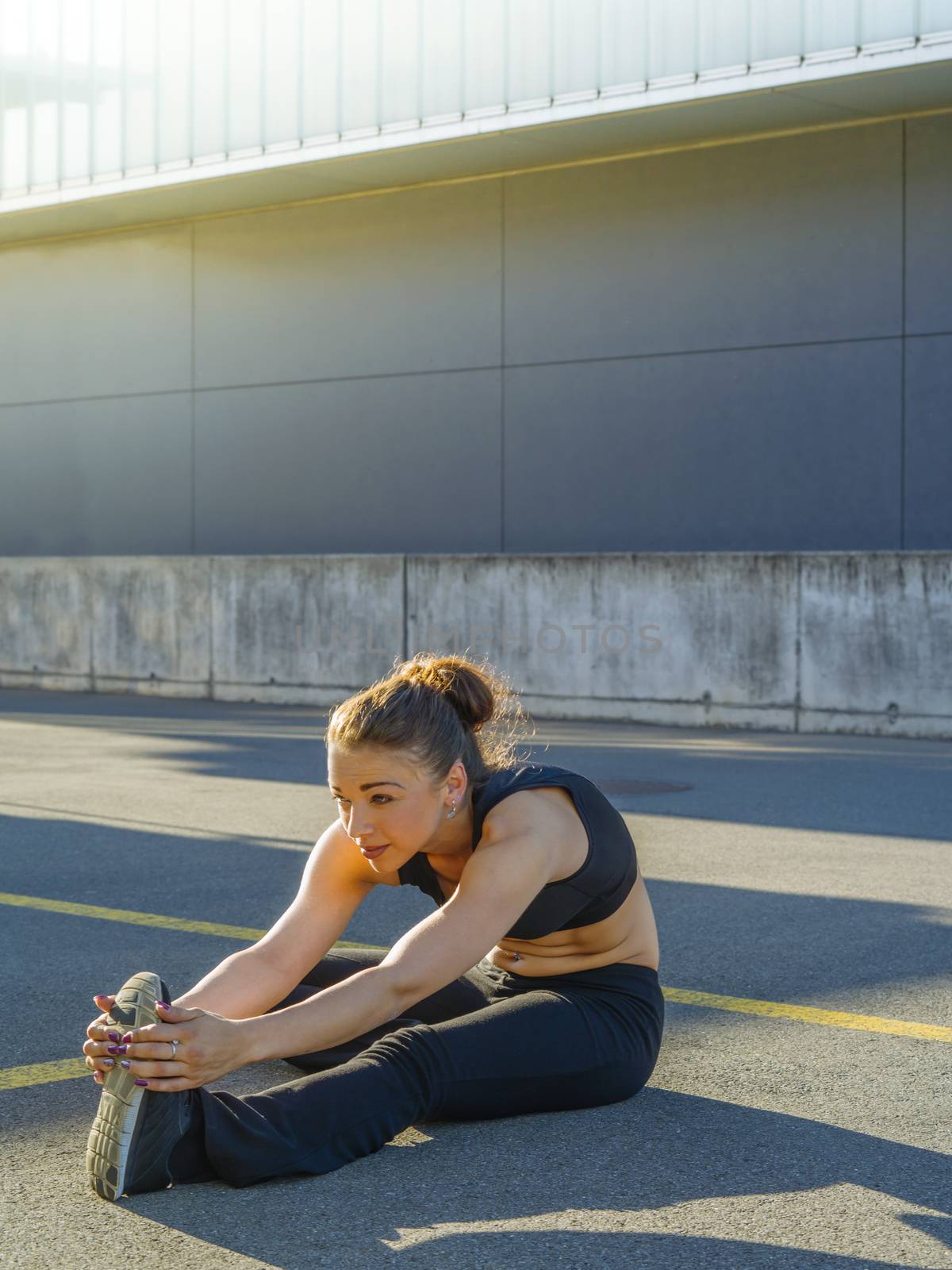 Photo of a woman in the city in the morning stretching her leg before her run.
