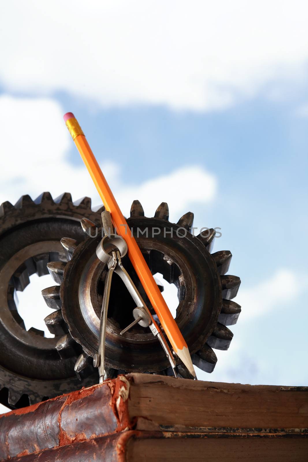 Divider near gears on stack of old books against blue sky background