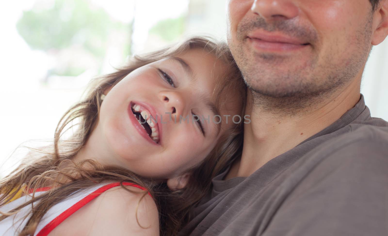 Close-up of a young smiling girl embraced by her father.