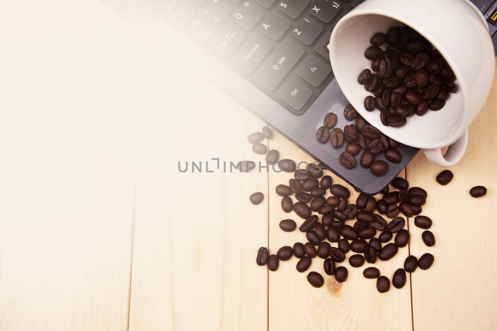 A cup of coffee put on table on laptop and spread coffee beans