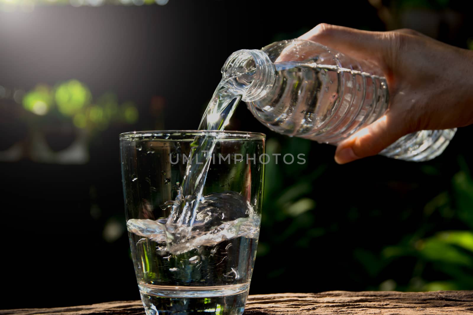 Female hand pouring water from bottle to glass on nature background