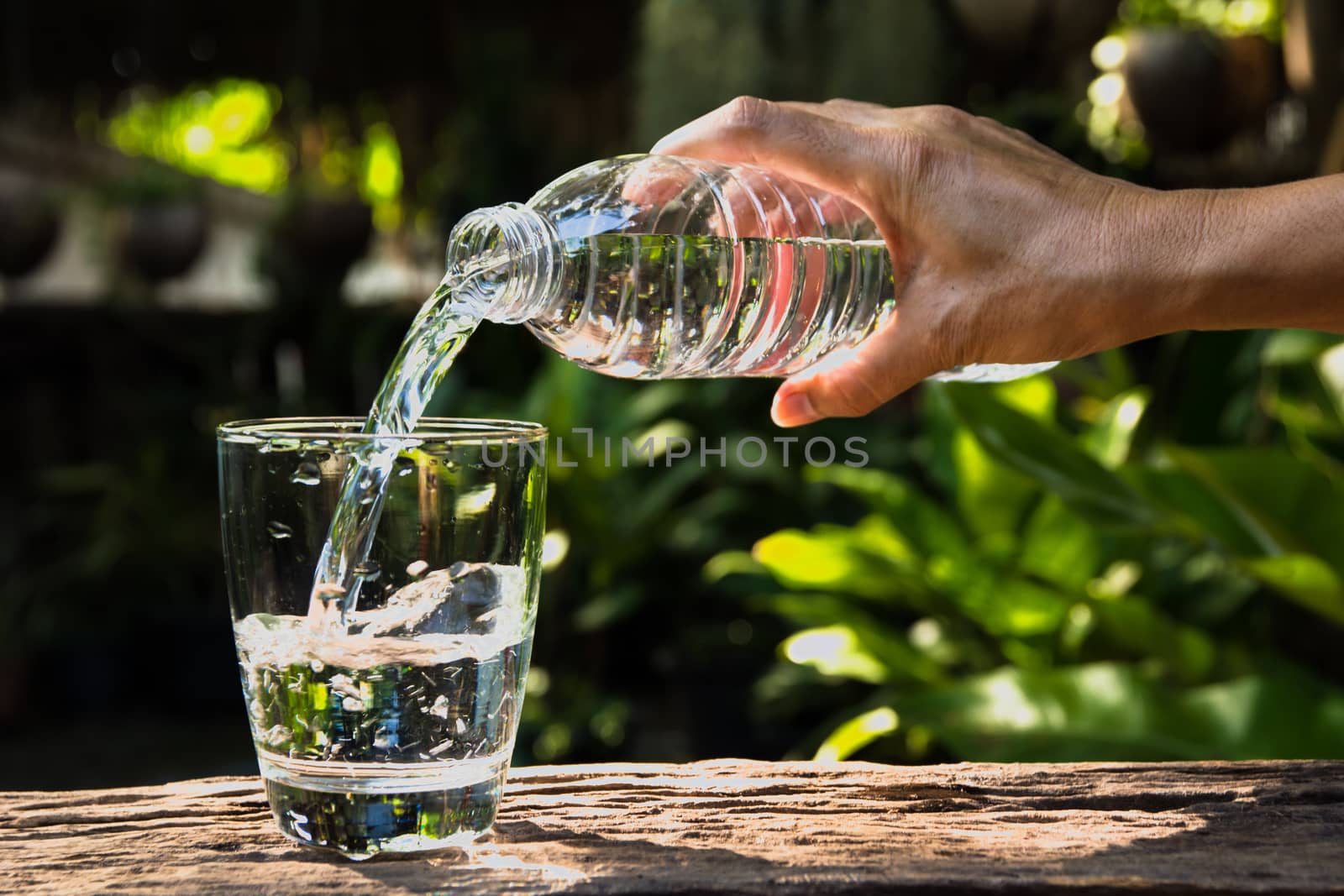 Female hand pouring water from bottle to glass on nature backgro by kirisa99