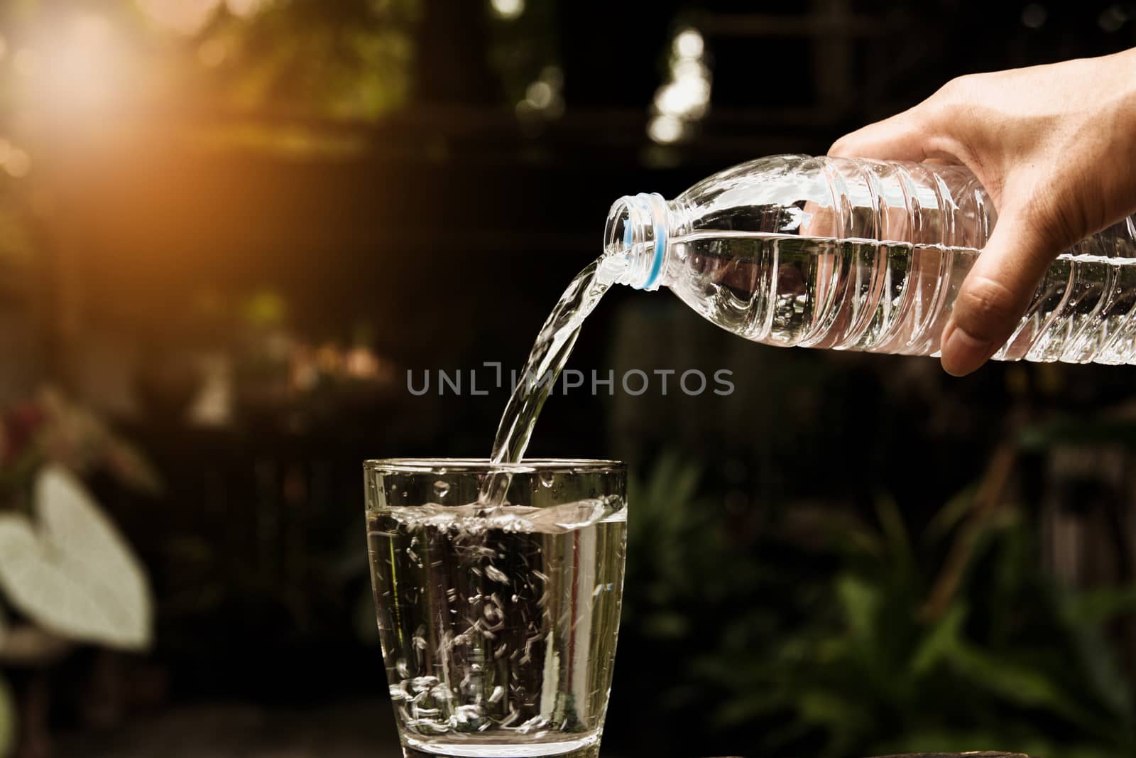 Female hand pouring water from bottle to glass on nature backgro by kirisa99
