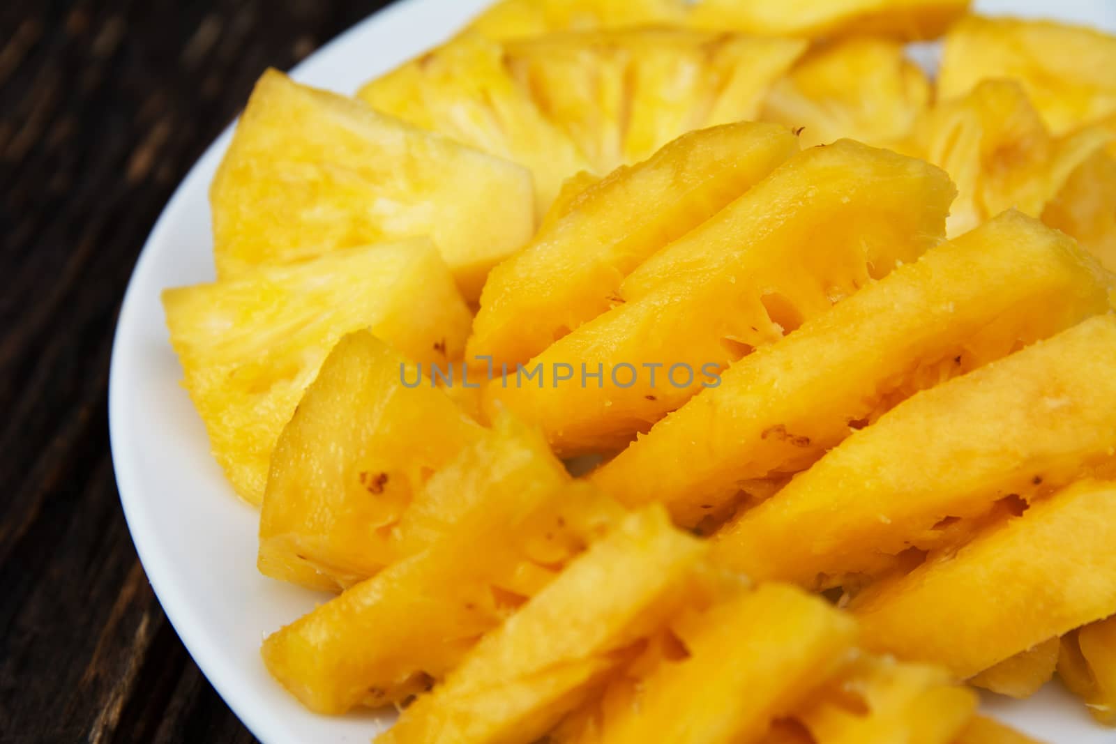 Sliced pineapple on the white plate on wooden table by kirisa99