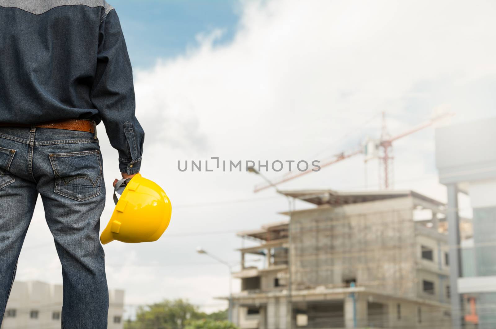 Engineer or safety officer holding yellow helmet with the building is background in construction site.