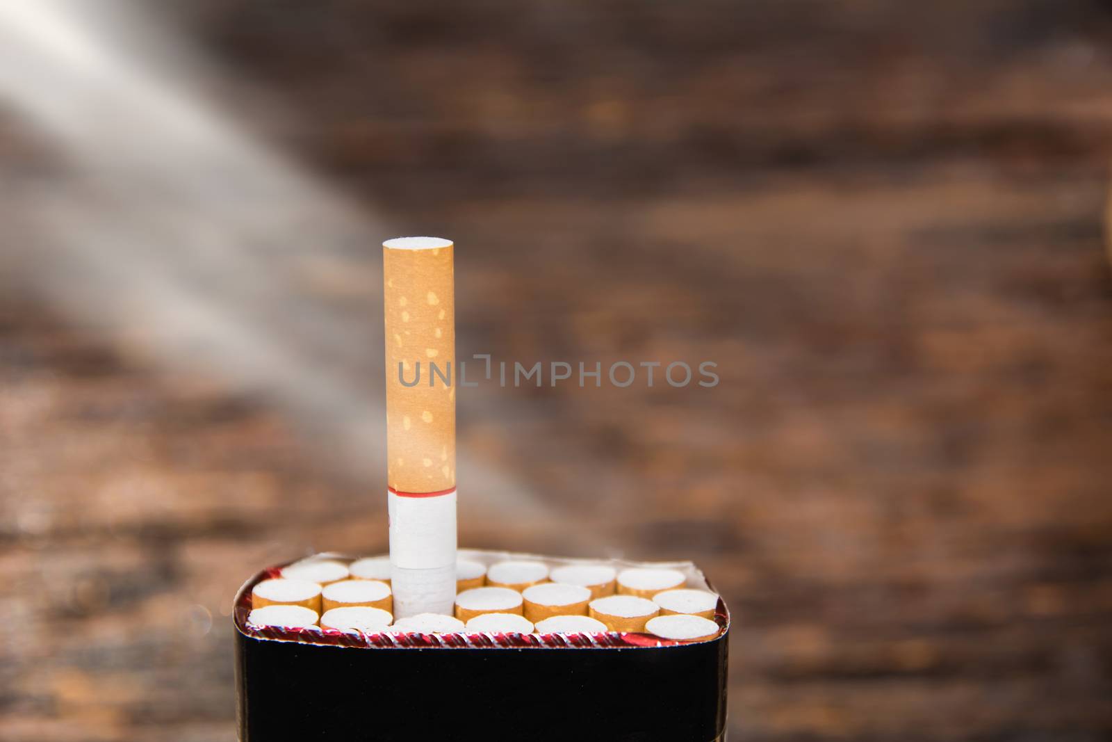 cigarette and cigarette box with sun ray on wooden background by kirisa99