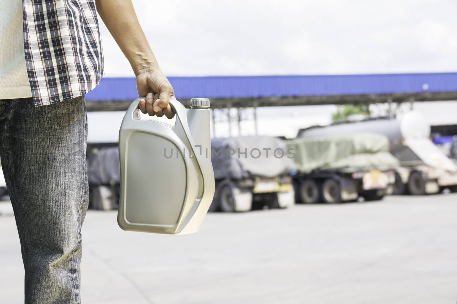 Hand of male holing gray plastic canister of motor oil on gas station background