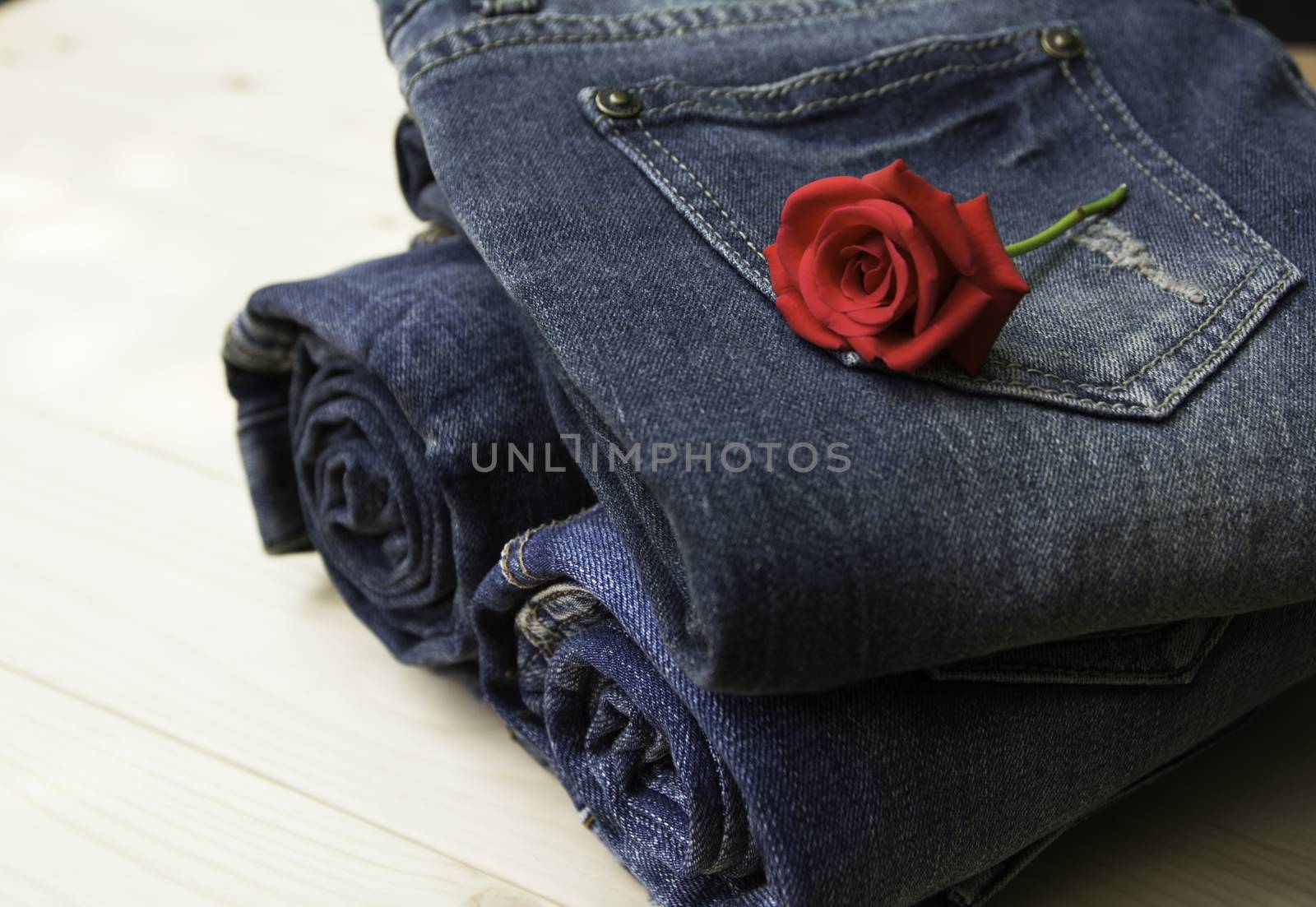 Blue jeans folded with red rose on wooden table and on wooden background.