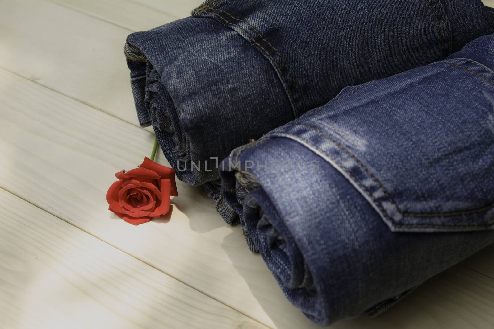 Blue jeans folded with red rose on wooden table and on wooden background.