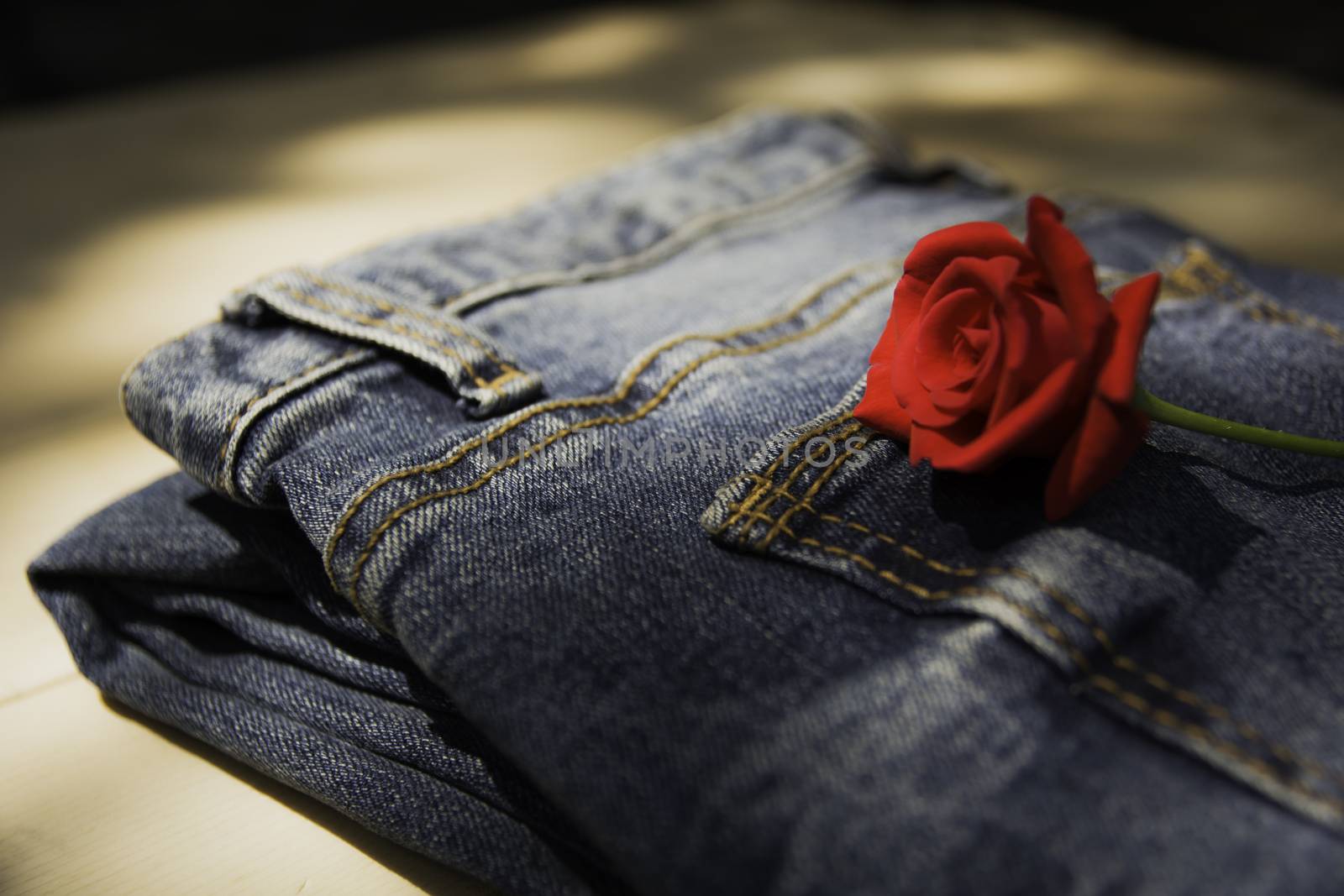 Blue jeans folded with red rose on wooden table and on wooden ba by kirisa99