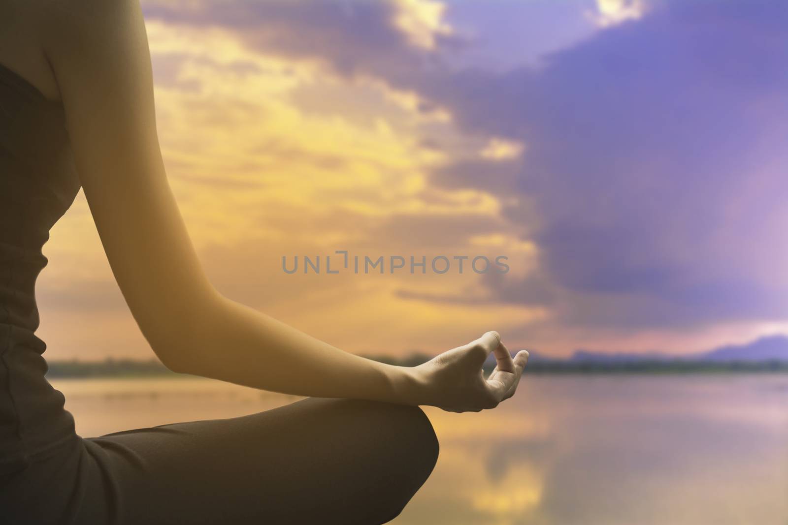 Close-up of feminine and masculine arms and crossed legs during meditation on river with sky background.