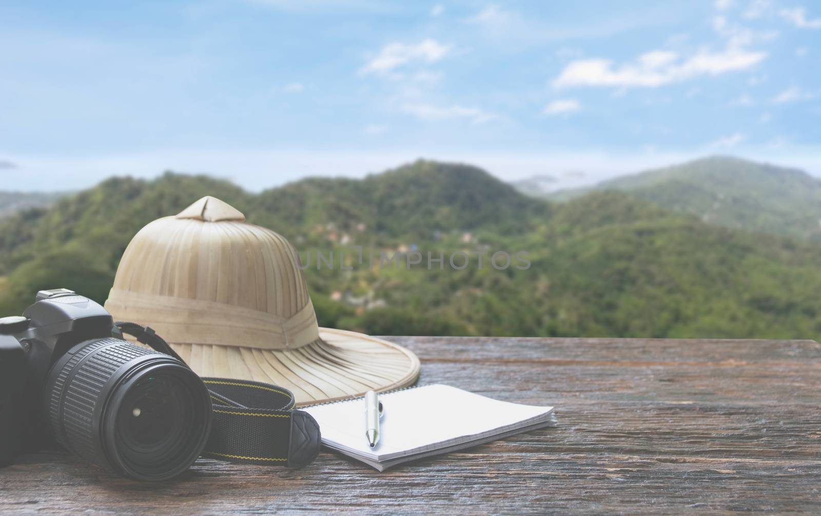 Camera with cap, notebook and pen on wooden table with mountain and sky background, Travel concept. Travel Accessories.