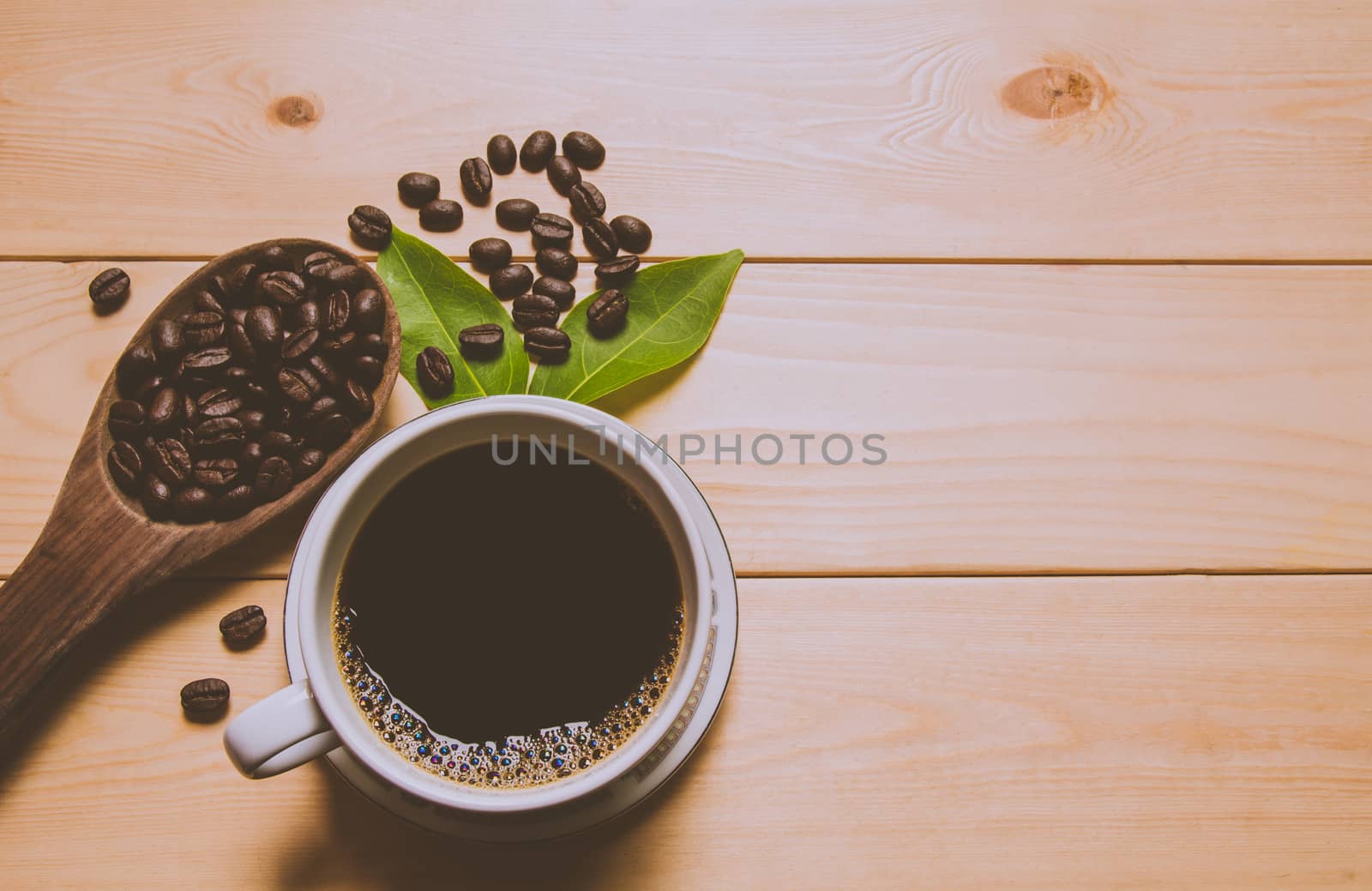 A cup of coffee with coffee beans and leaf over wooden table. Top view. Copy space.