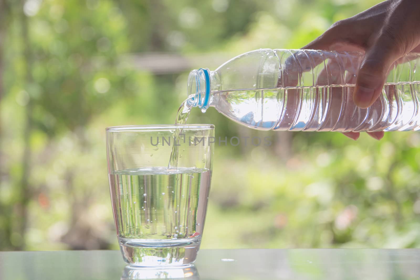 Female hand pouring water from bottle to glass on nature background