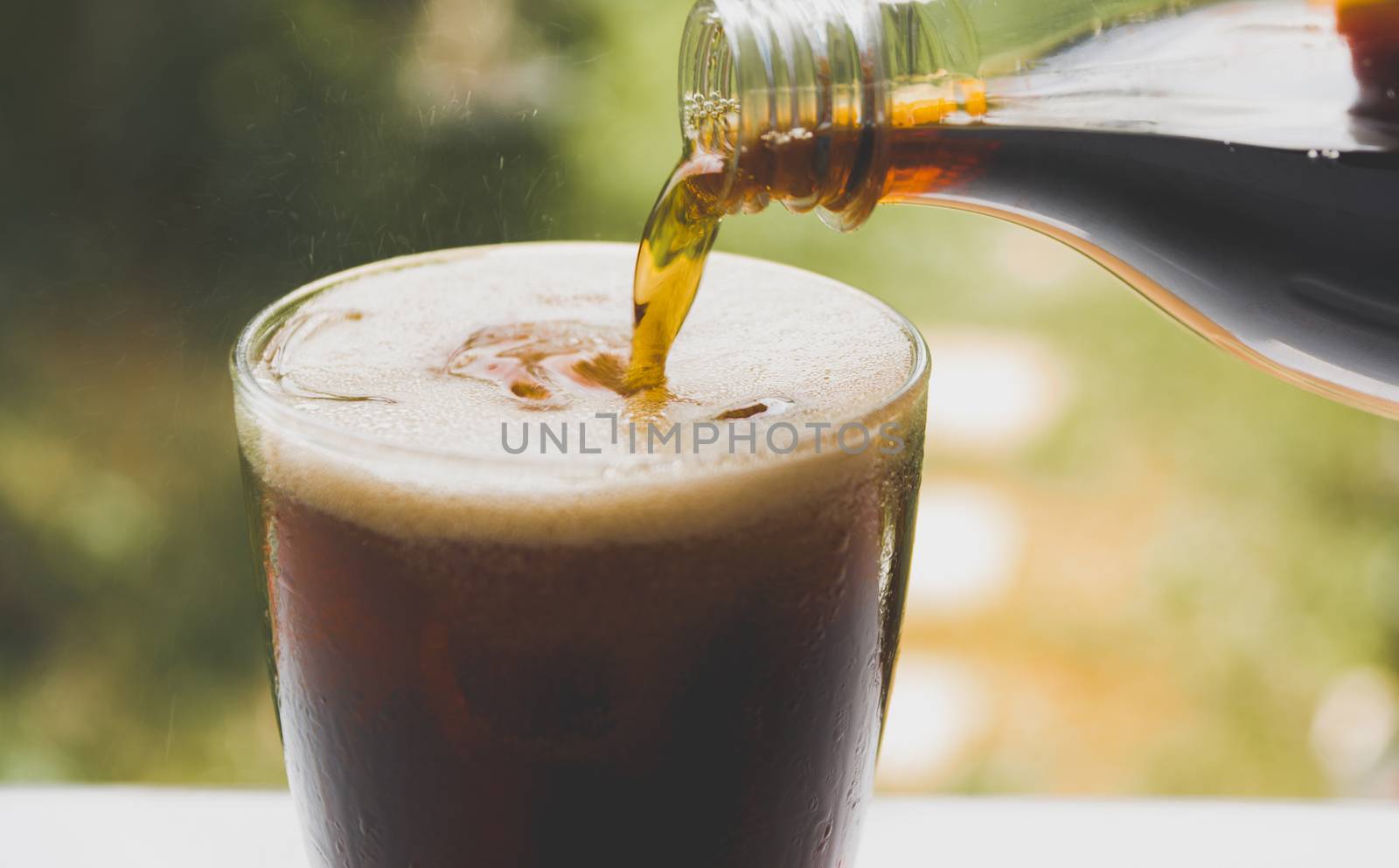 Person pouring water soda from bottle to glass on nature background