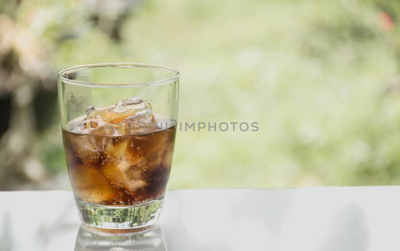 Water soda and ice cube in the glass on table with nature background