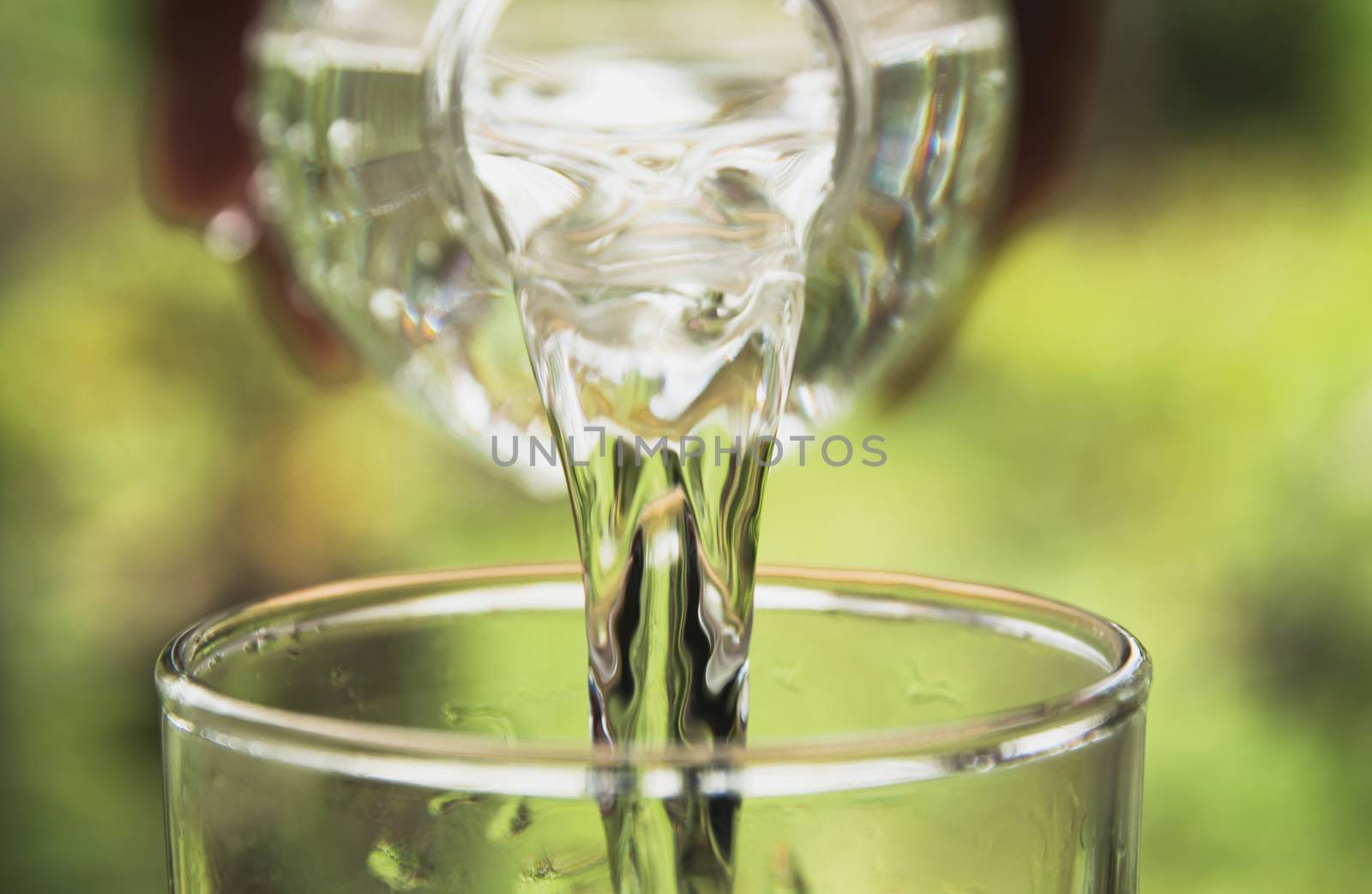 Person pouring water from bottle to glass on nature background