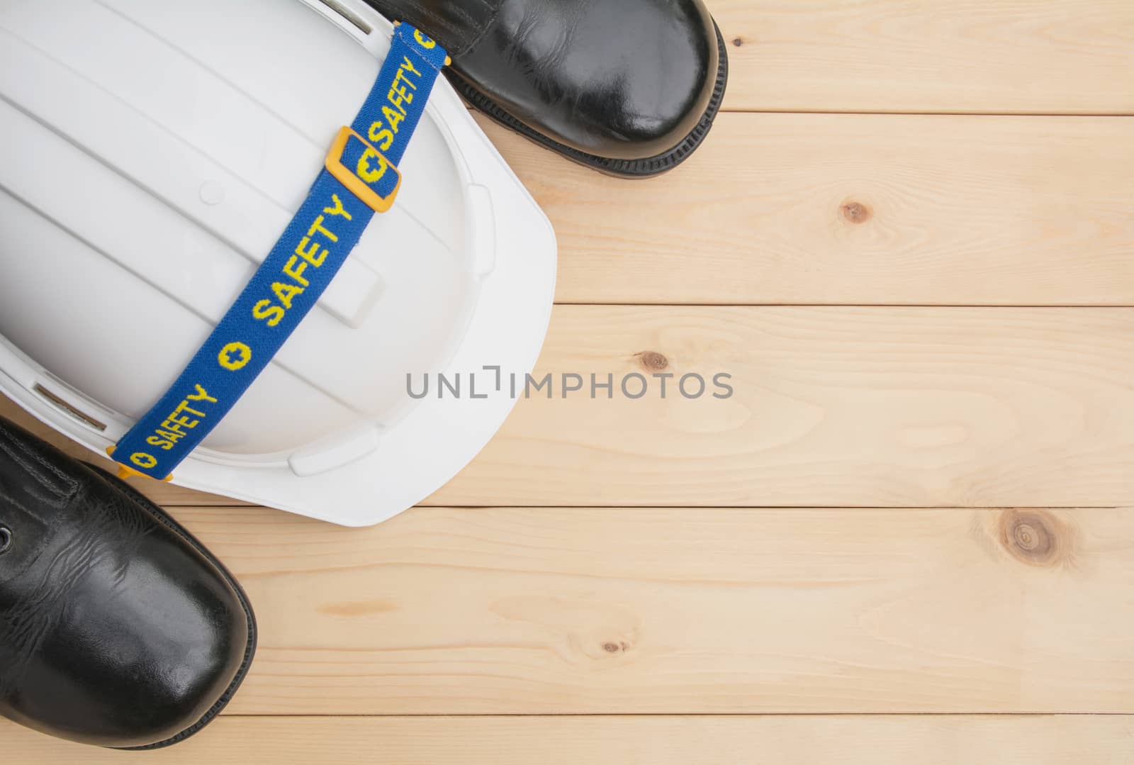 White plastic safety helmet with leather footwear on wooden desk with copy space.