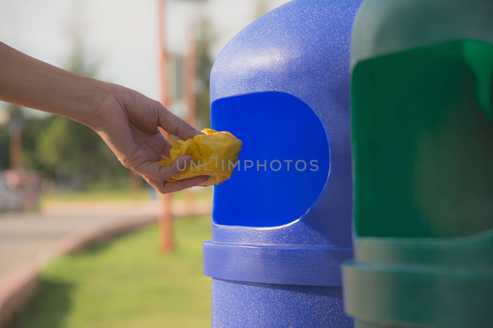Female hand throwing crumpled yellow plastic into blue plastic trashcan.