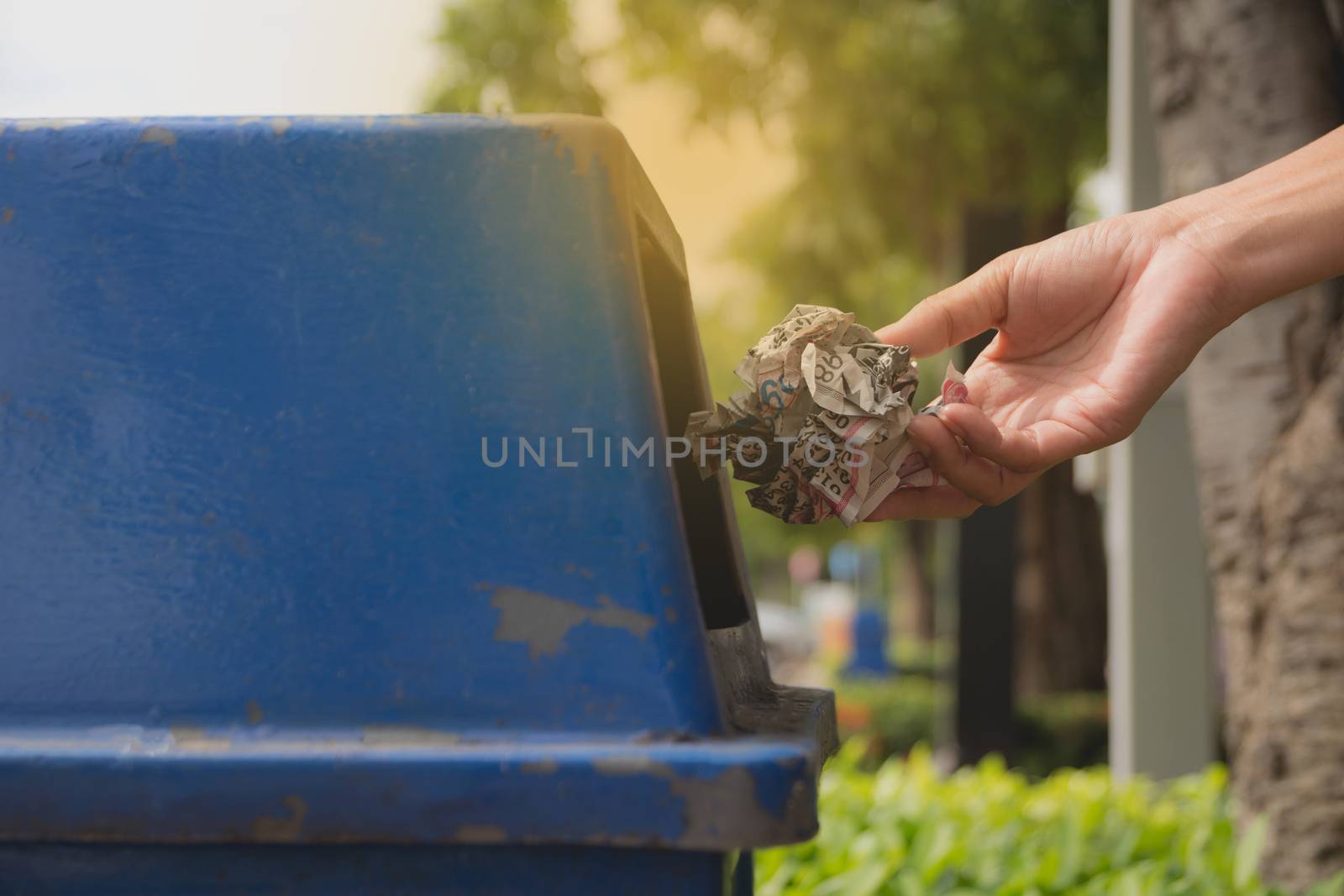 Female hand throwing crumpled paper into blue plastic trashcan. by kirisa99