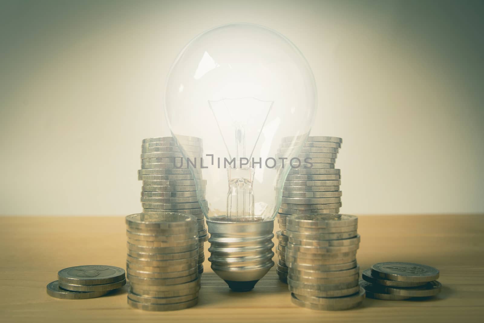 Energy saving light bulb and surrounding by stacks of coins on wooden table.