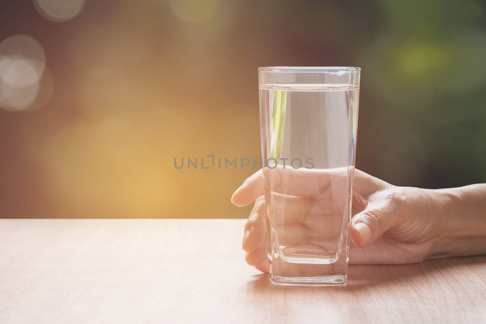 hand holding a glass of pure water. Hand holding a glass of water on table with nature background.