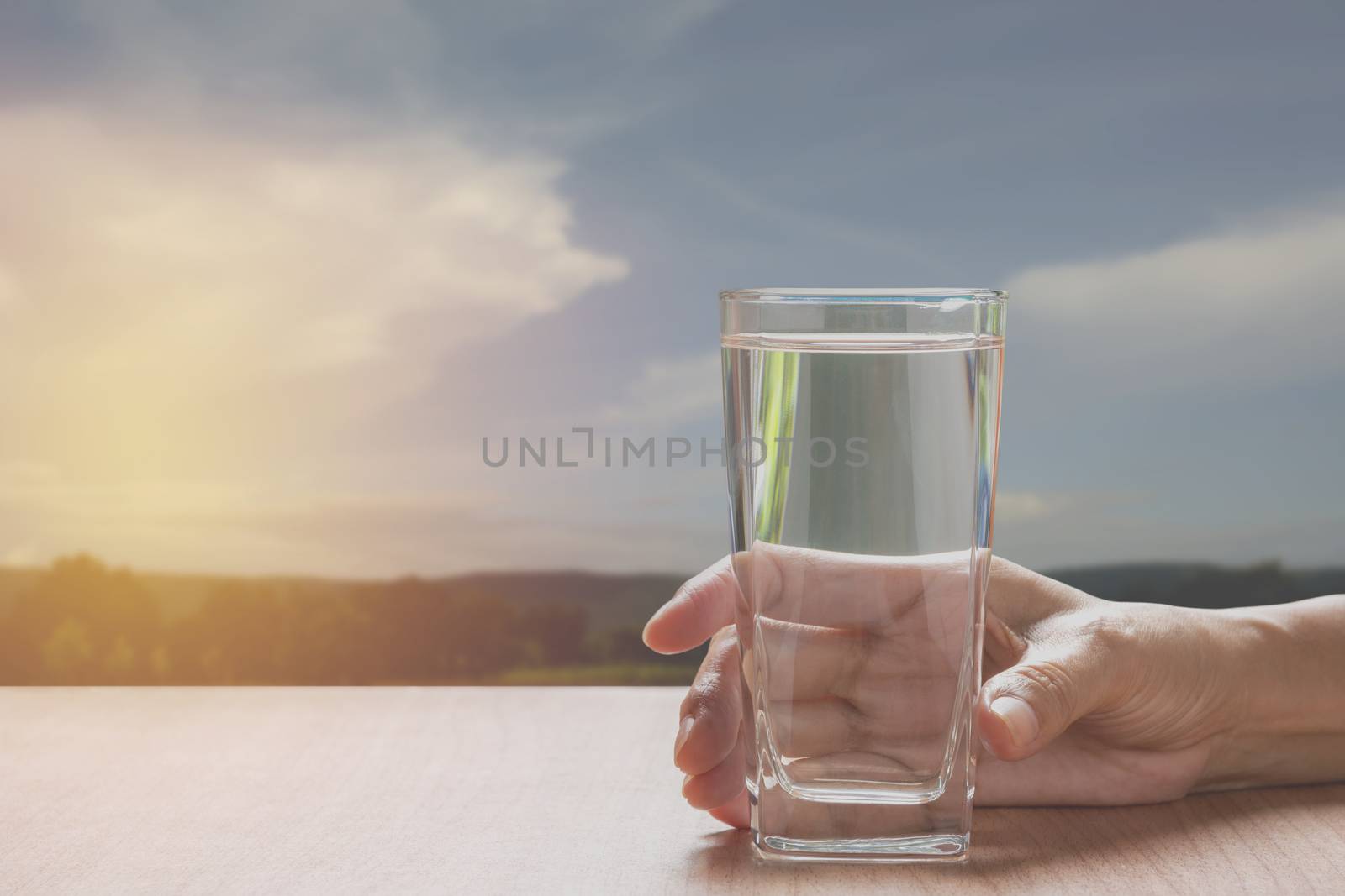 hand holding a glass of pure water. Hand holding a glass of water on table with blue sky background.