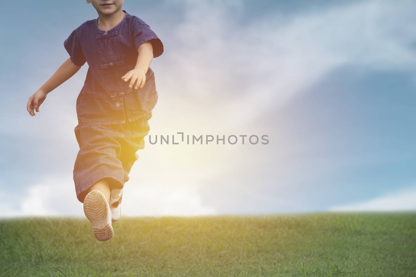 Kid running and playing have fun and joy at the grass field under the blue sky.