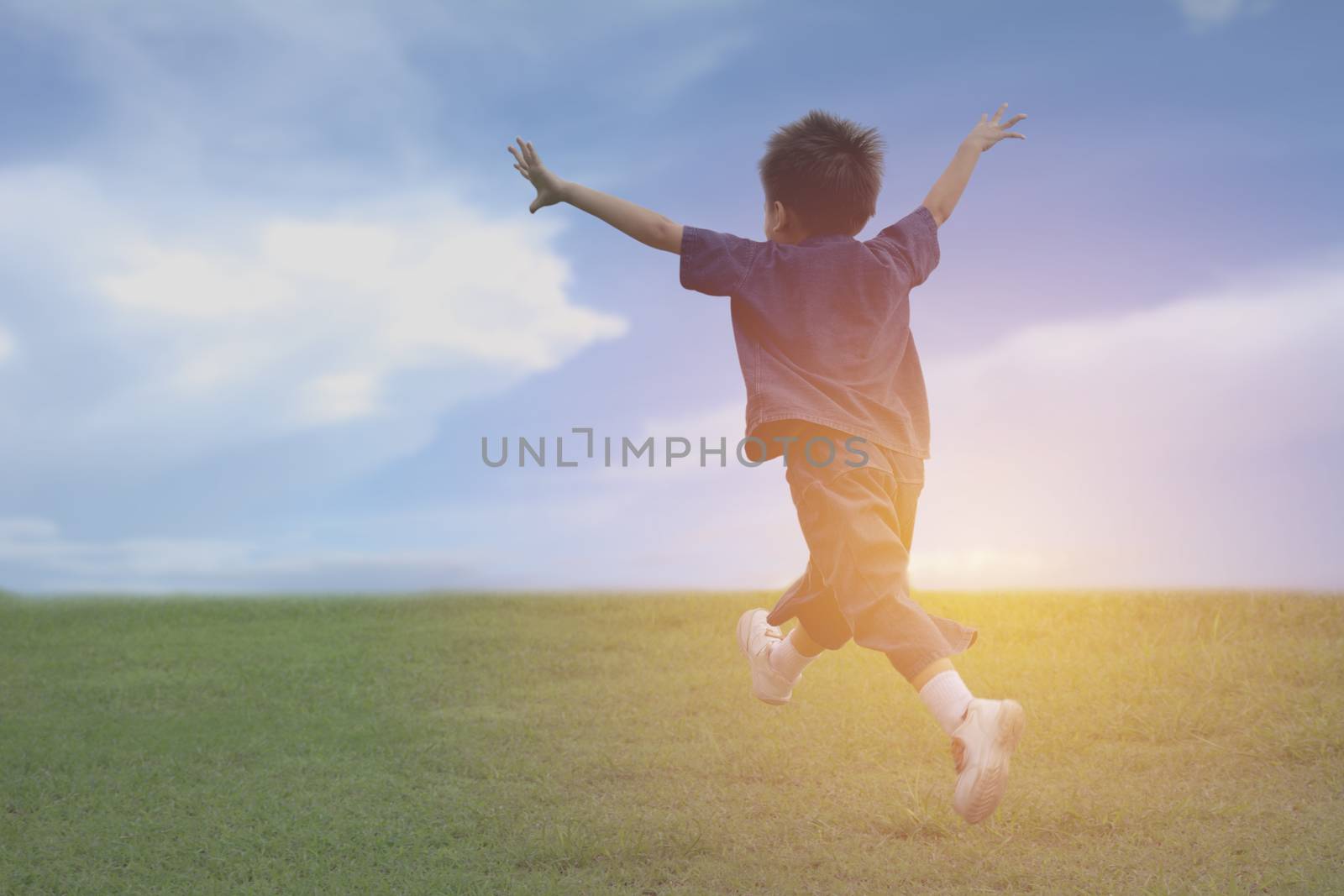 Kid running and playing have fun and joy at the grass field under the blue sky.