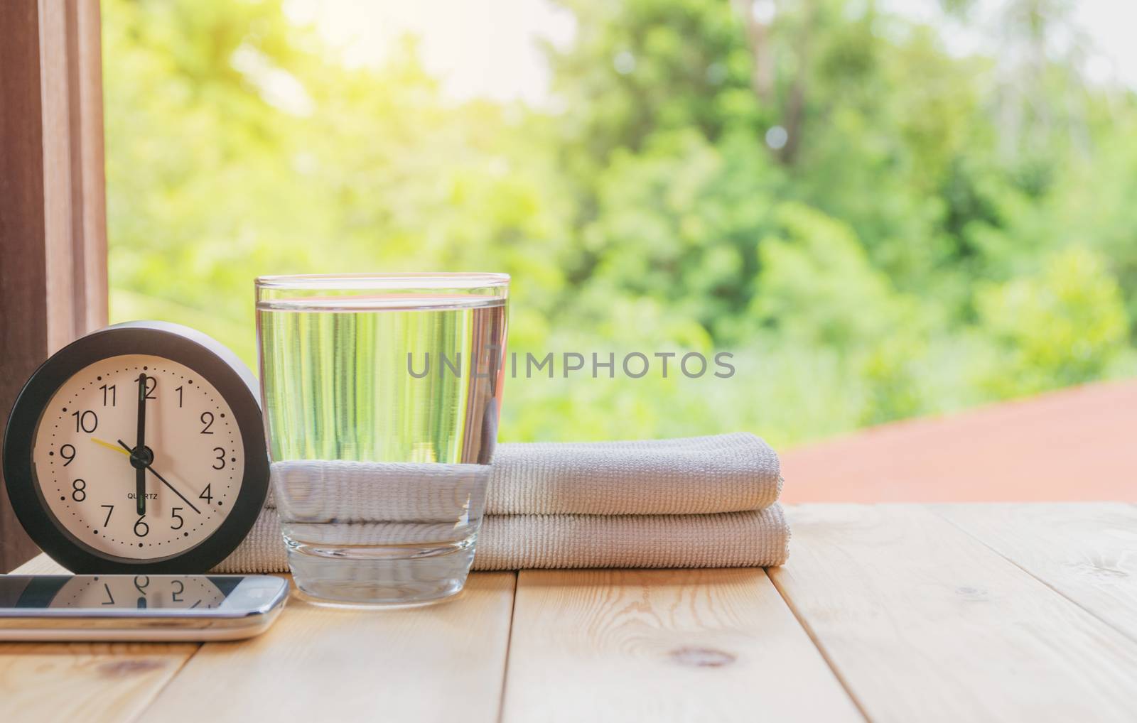 glass of water on a wooden table with clock and handkerchief on nature background.