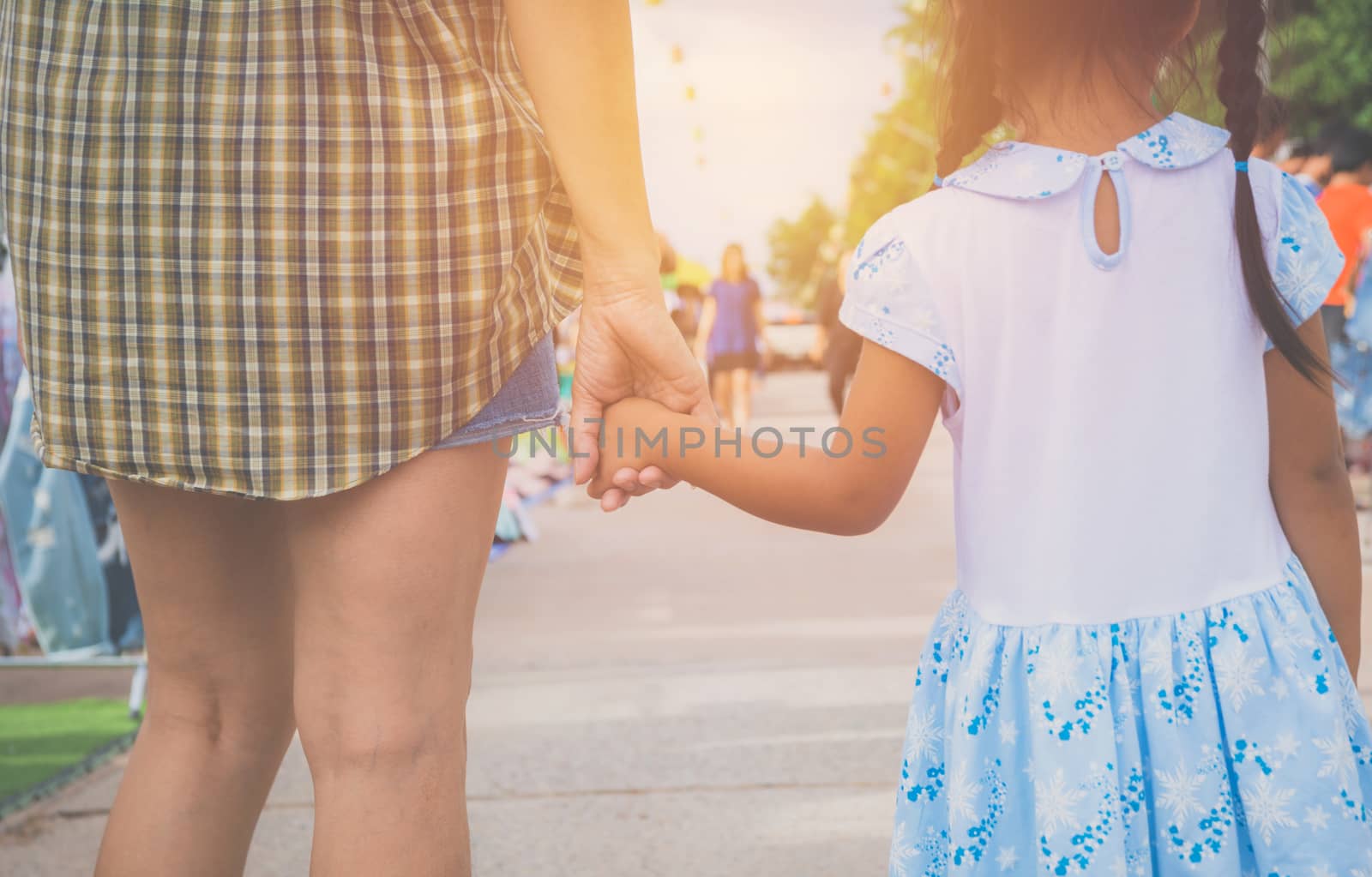 Mom with little daughter walking together on the way at the sunset.