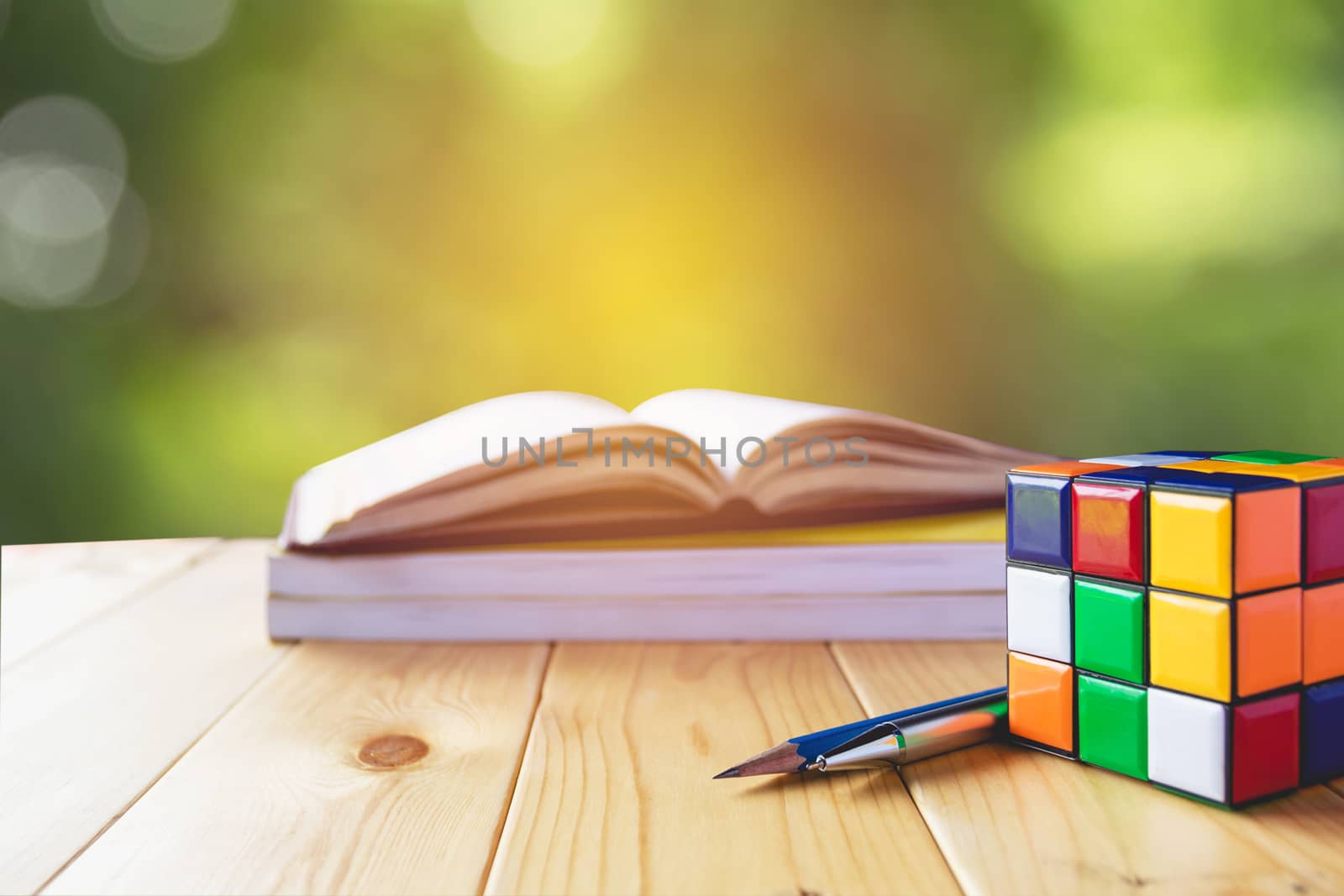 Rubik cube, book, pen and pencil in wooden table on nature backg by kirisa99