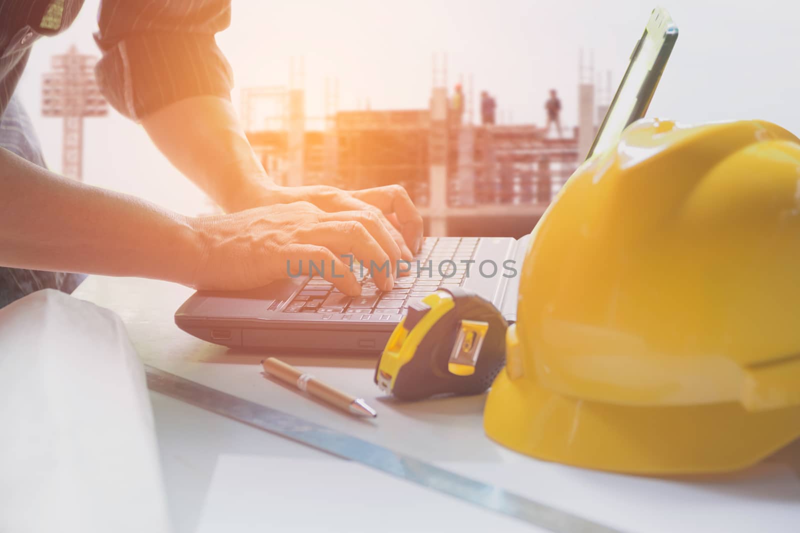 Architect engineer using laptop for working with yellow helmet, laptop and coffee cup on table.