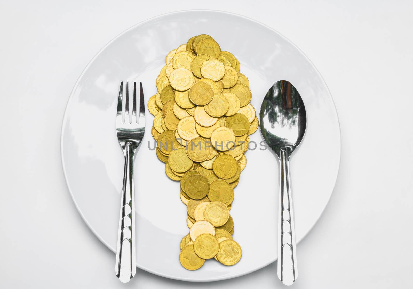 Golden coins shape fish with spoon and fork on white plate and white table.