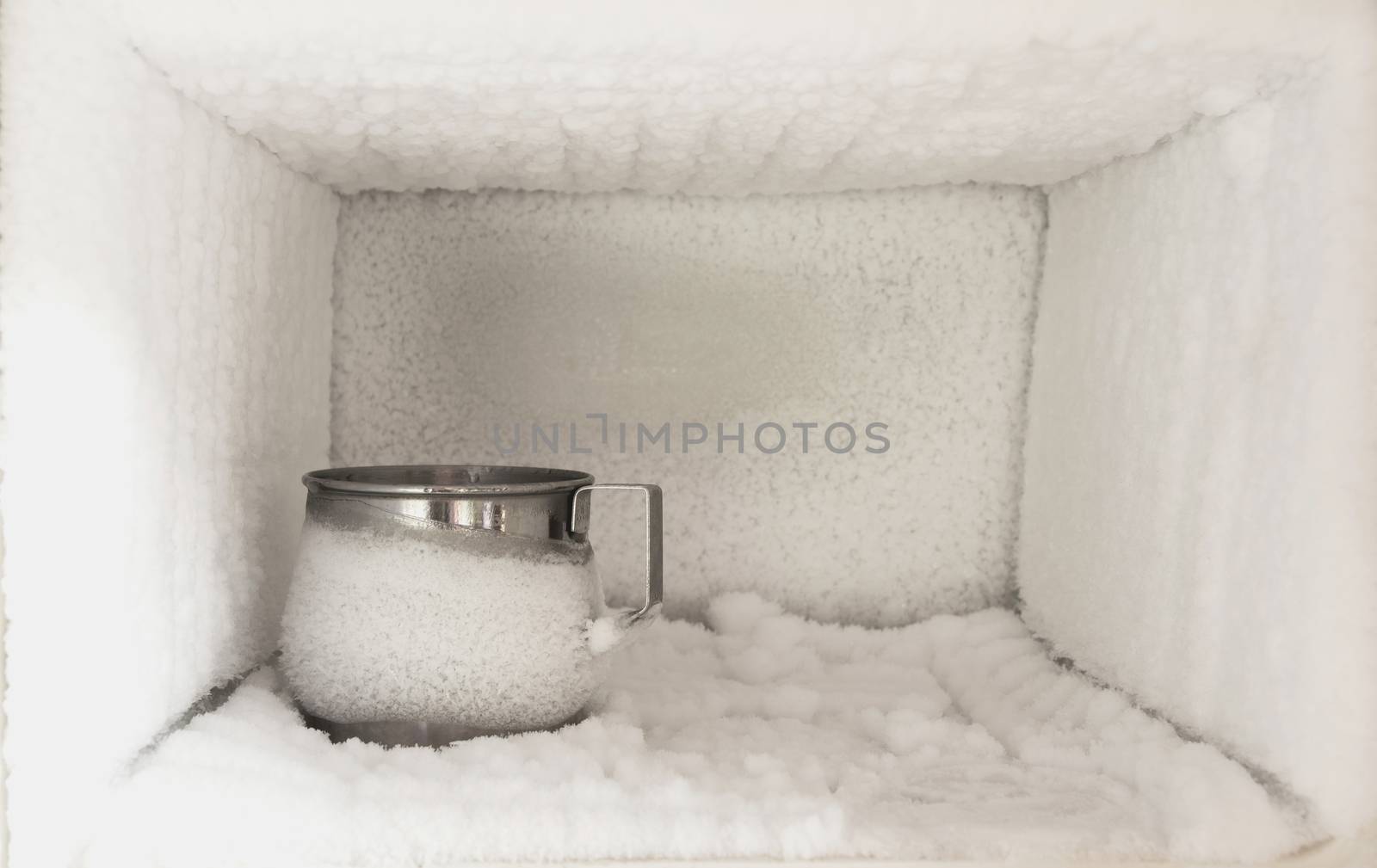 Stainless steel drinking water glass in freezer of a refrigerator. Ice buildup inside of a freezer walls.