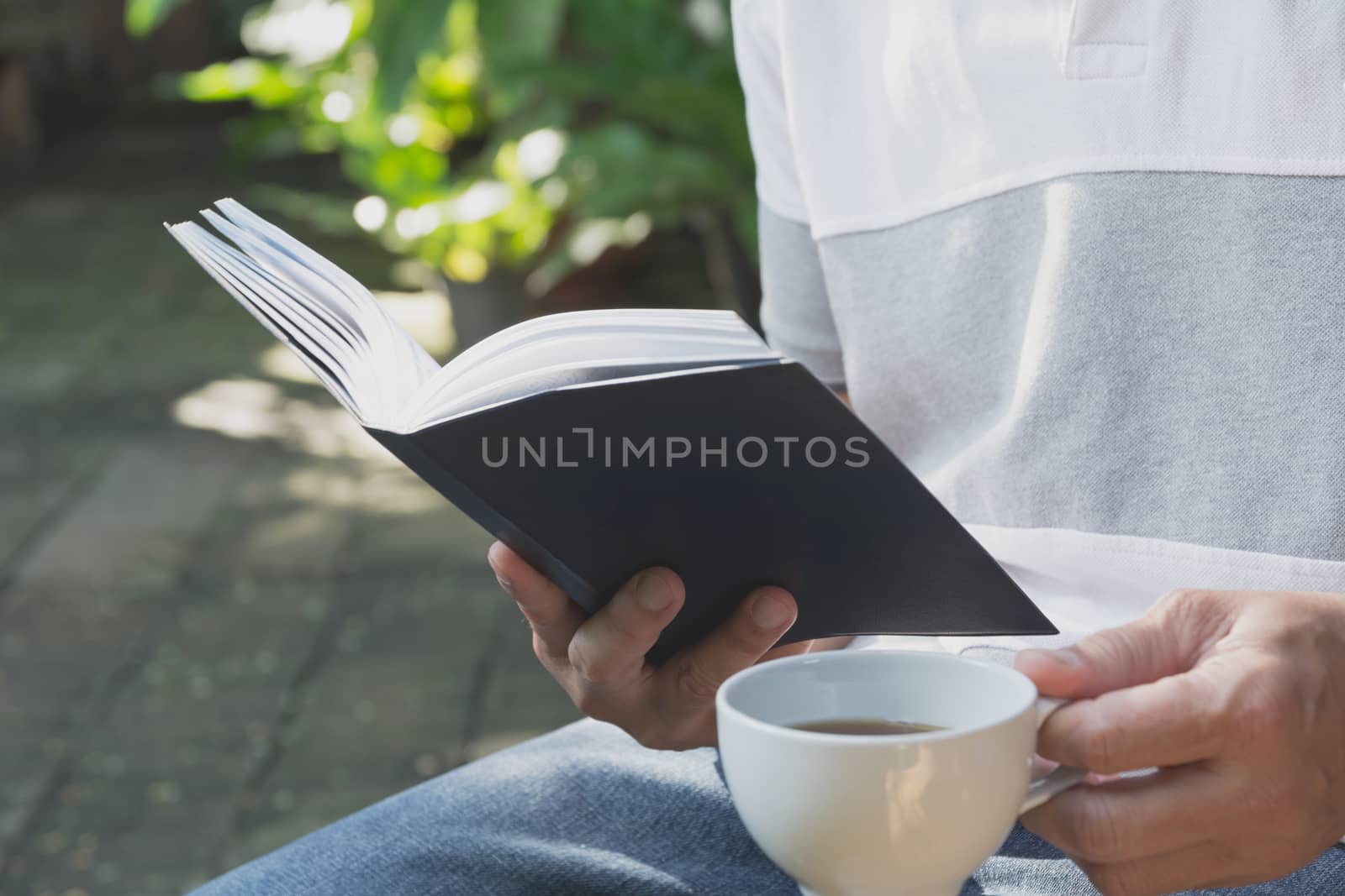 Portrait man wearing T-shirt .Man stay in the park for reading book and drinking coffee.