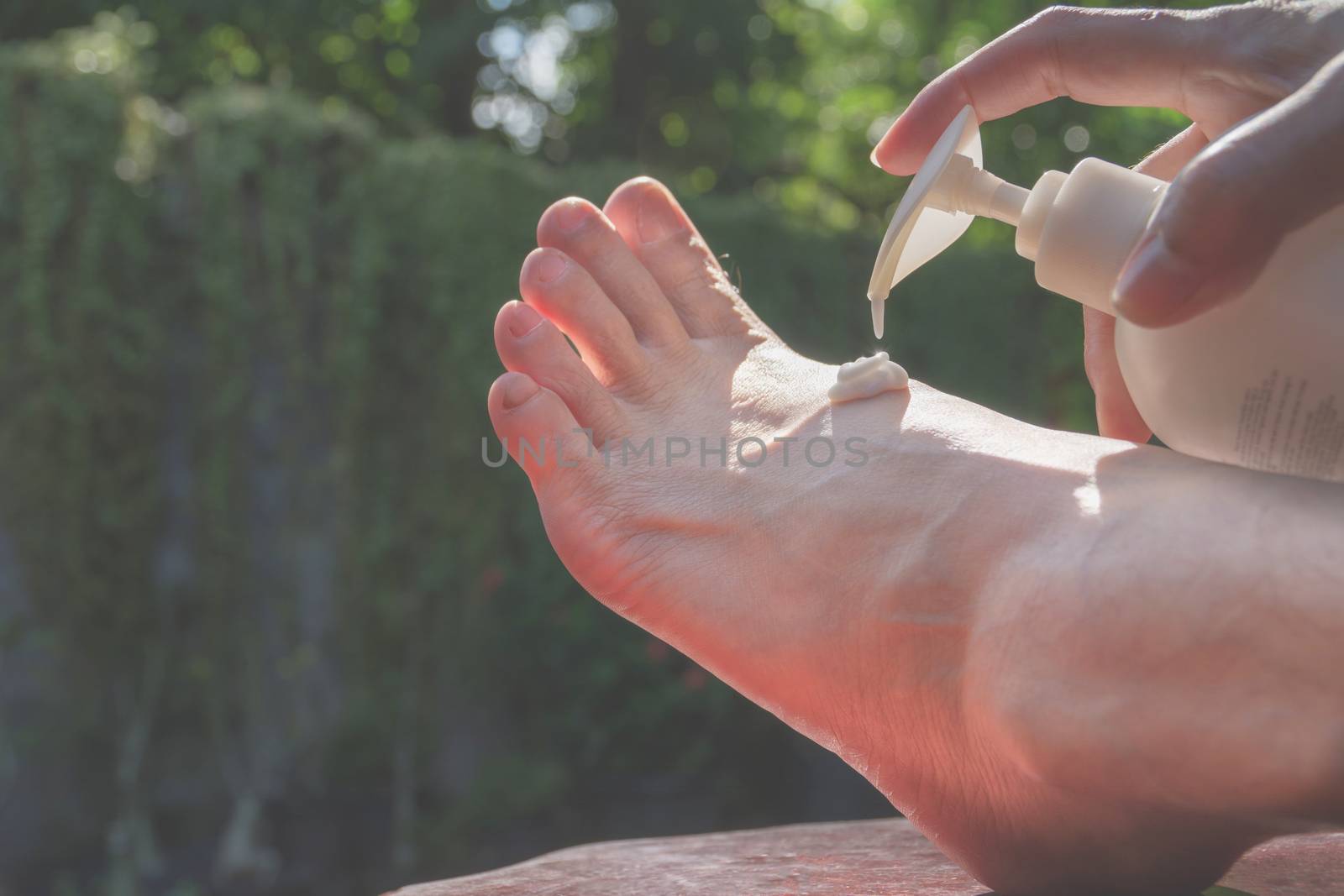 hand of woman apply lotion on skin of back foot on nature background.