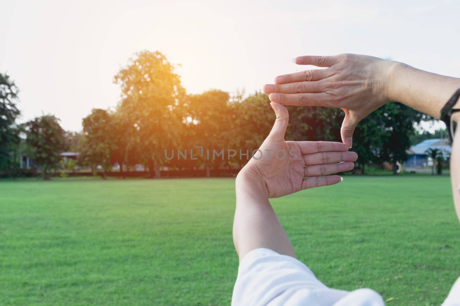 Close up of hands making frame gesture. Sunny spring sunset. Photo frame hands made by woman.