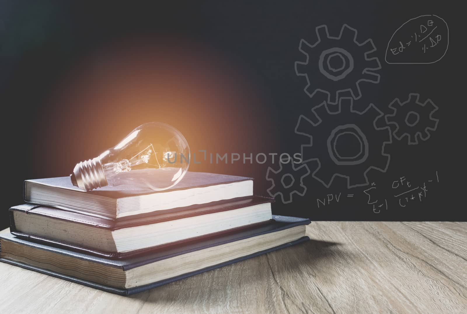 Pile of book with glowing light bulb over it on wood wall background. Knowledge, education concept.