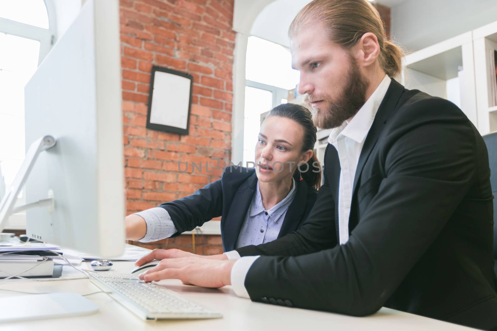 Two business people using computer together in office pointing at monitor