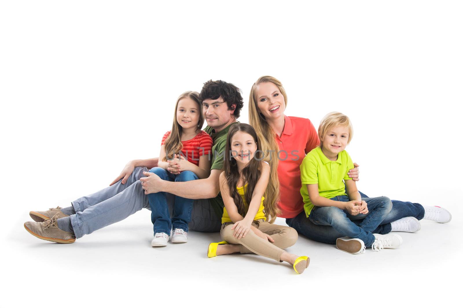 Happy smiling family of two parents and three children sitting on the floor studio isolated on white background