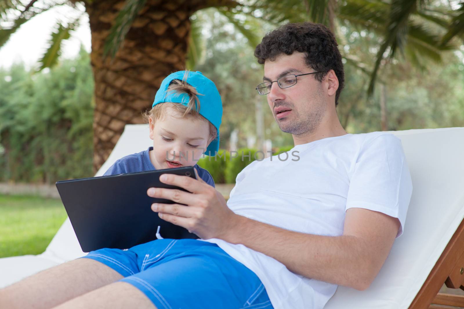 Young father showing something on tablet to his little boy outdoors.