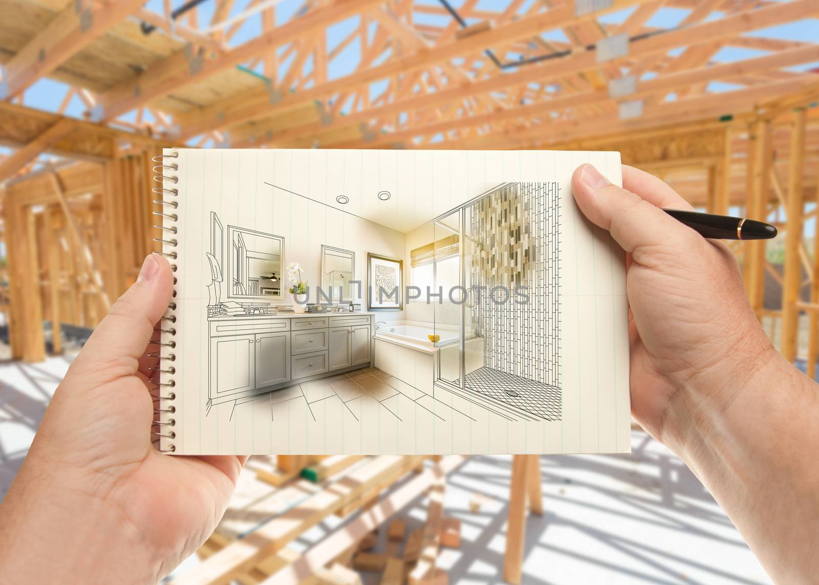 Hands Holding Pen and Pad of Paper with Bathroom Design Inside House Construction Framing. by Feverpitched