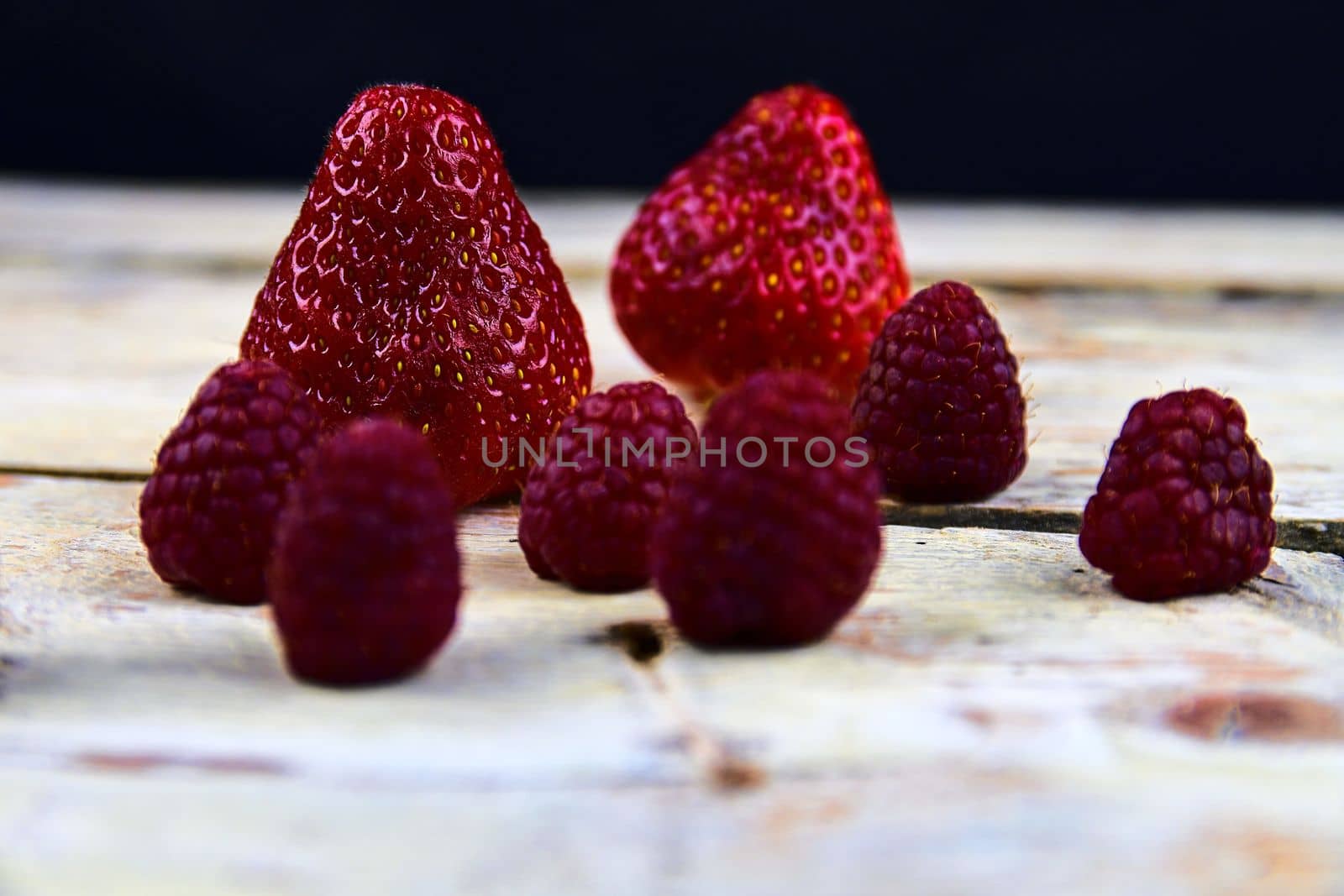 Strawberries and raspberries on rustic white wooden background. White and black background. Dark image. 