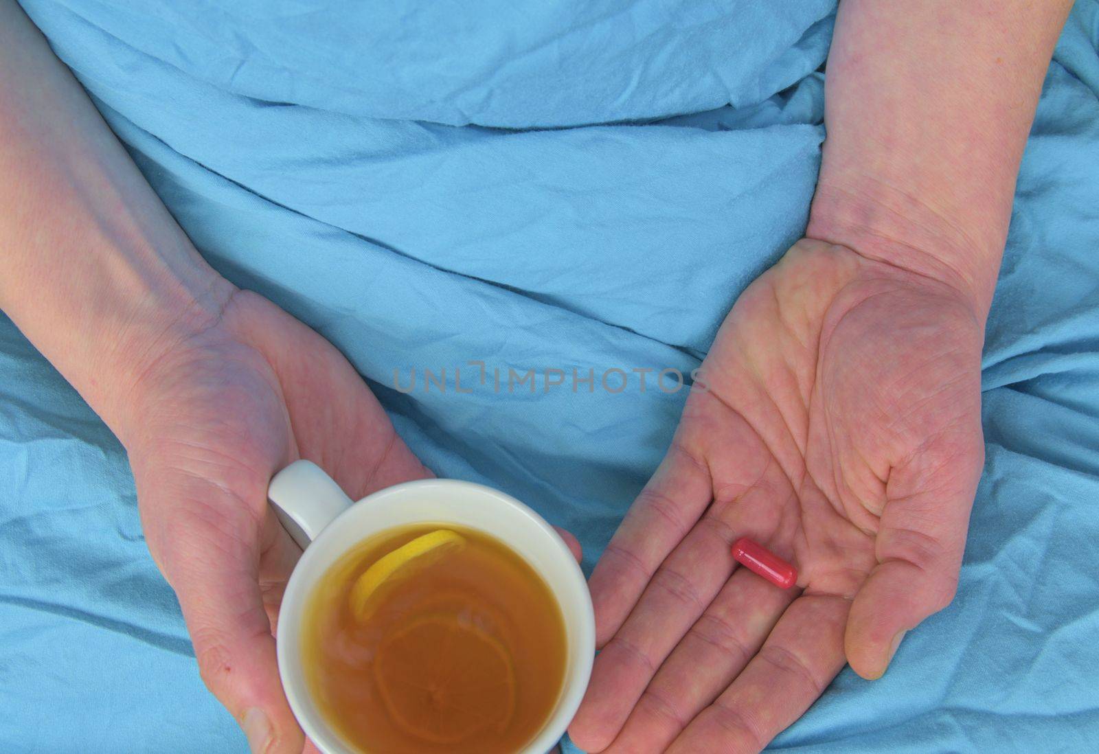 Ill man with fever drinking cup of warm tea and taking pill. Influenza season. Hands of the sick man holding pill and cup of the hot tea in the bed. Close-up of ill caucasian man at home by roman_nerud