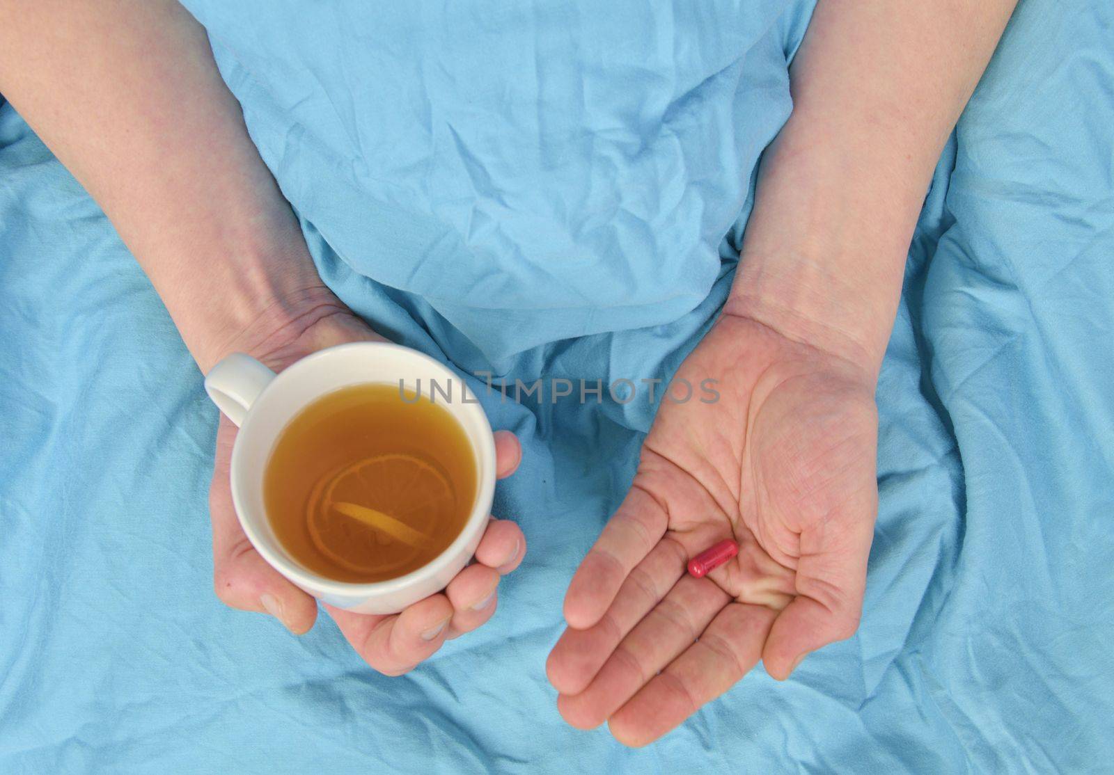 Ill man with fever drinking cup of warm tea and taking pill. Influenza season. Hands of the sick man holding pill and cup of the hot tea in the bed. Close-up of ill caucasian man at home.